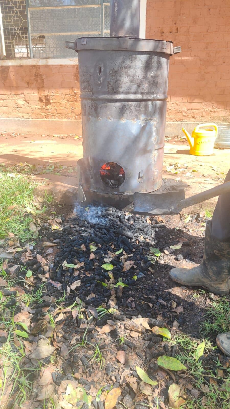 A trainer crouching next to the kiln, inspecting pieces of biochar